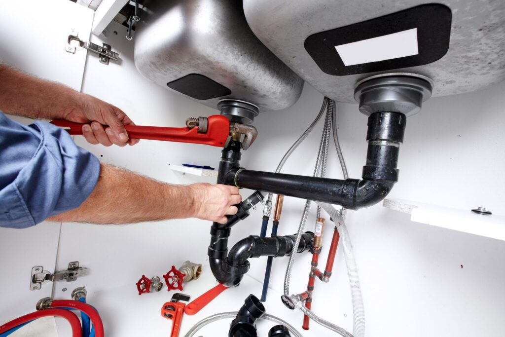 Plumber repairing drain pipes beneath a kitchen sink in Boynton Beach